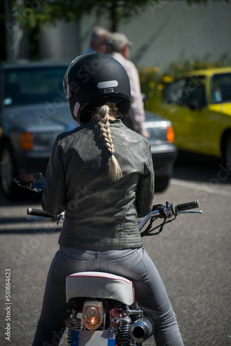 Portrait on back view of blond girl sitting on vintage motorbike in the street