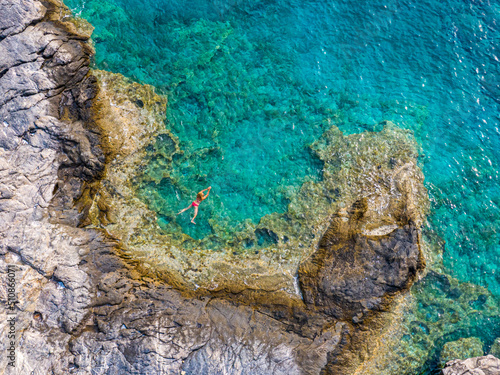aerial view of transparent sea surface with unrecognizable people swimming in the sea, Amorgos, greece
