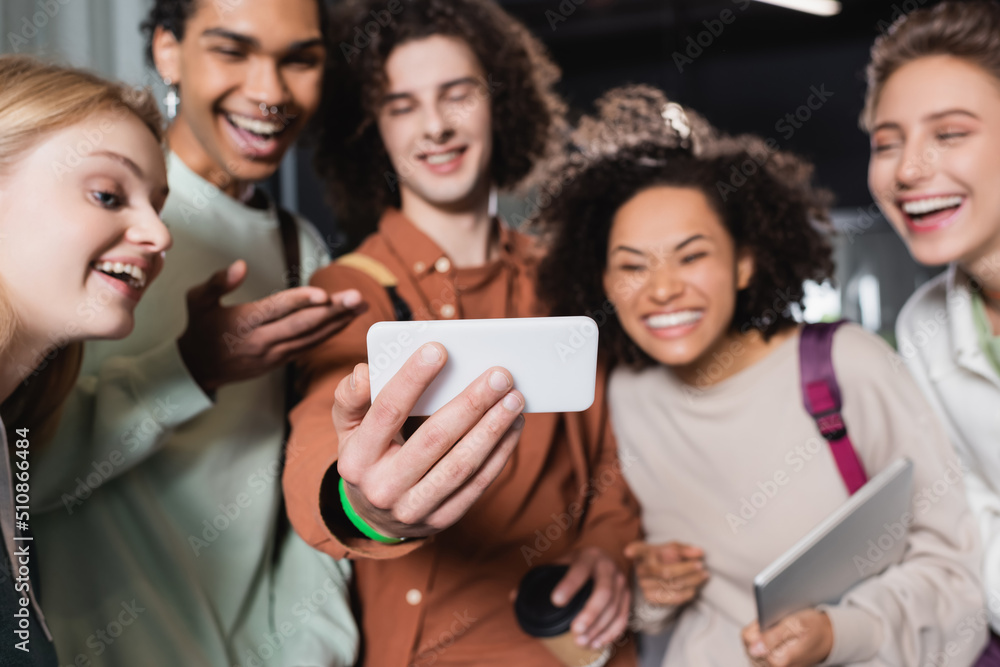 young man taking selfie on mobile phone with interracial students on blurred background. young man taking selfie on mobile phone with interracial students on blurred background.