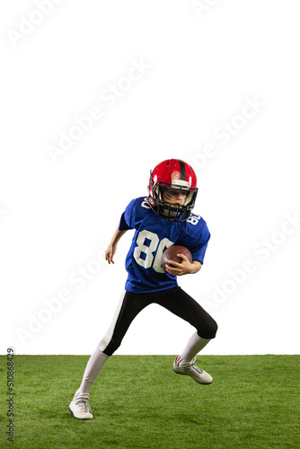 Sportive little boy in sports uniform and equipment playing american football isolated on white background with green grass flooring. Concept of sport, movement, achievements.