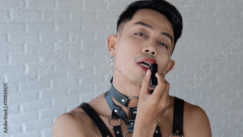 The passionate face of a handsome homosexual man who paints his lips with lipstick. LGBT community for the rights of sexual minorities. Asian model male gay transgender looking at the camera.