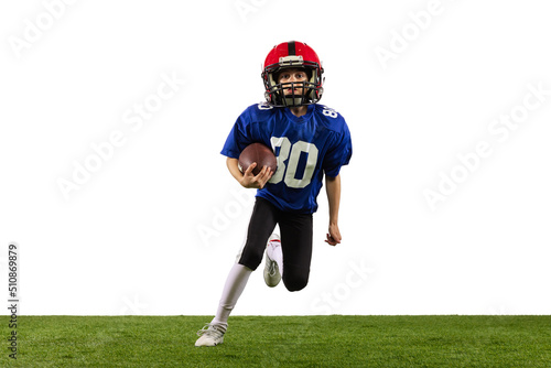 Dynamic portrait of little boy, beginner player of american football training isolated on white background with green grass flooring. Concept of sport, movement, achievements.