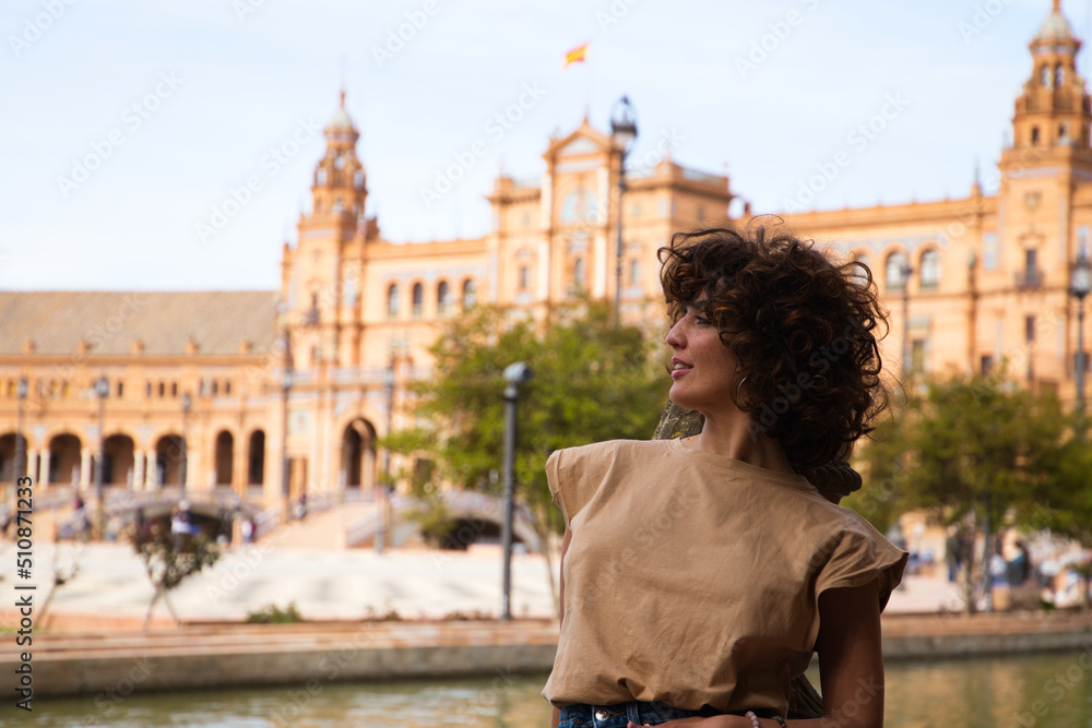 beautiful woman with curly hair is on holiday in sevilla. The woman is posing for pictures in front of the most famous square of the centuries old city. Holiday and travel concept.