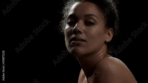 Wallpaper Mural Pretty young slim African American woman with black curly hair in bun and wet shoulders moves her head up and looks at the camera on black background | Skin moisturizing concept Torontodigital.ca