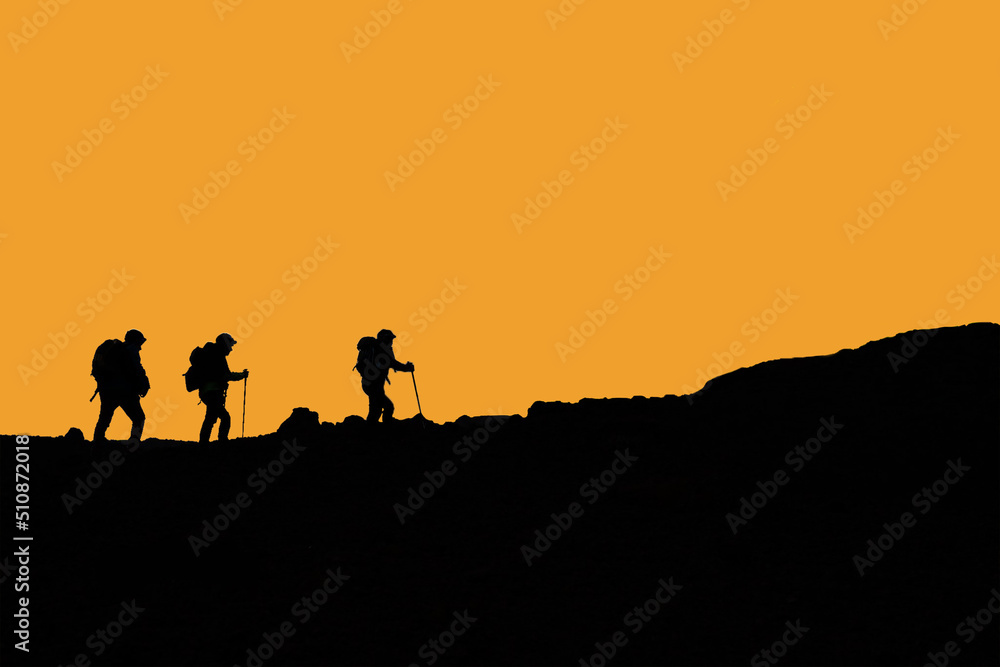 Silhouette escursionisti che camminano in montagna con cielo arancio
