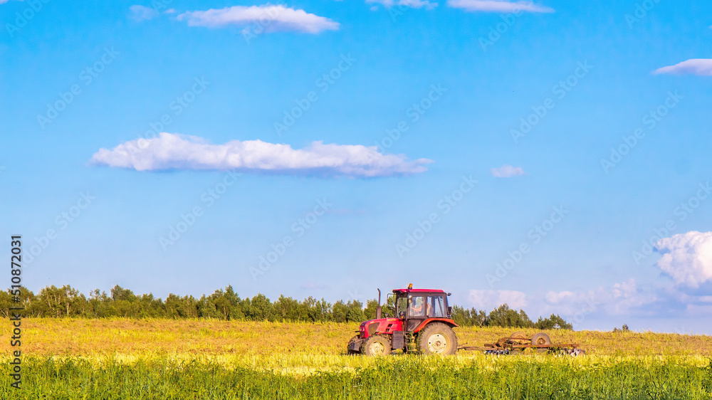 A red tractor plows a field on a summer day. Working day in agriculture A red tractor plows a field on a summer day. Working day in agriculture