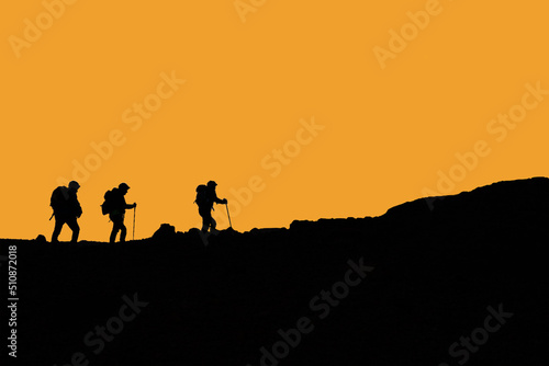 Silhouette escursionisti che camminano in montagna con cielo arancio 