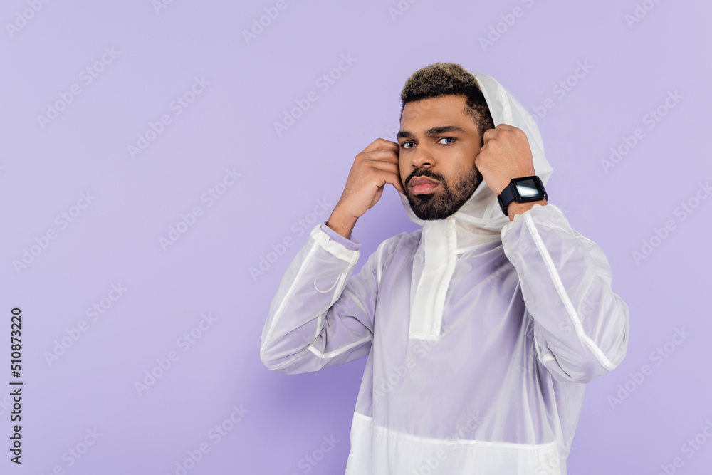 african american sportsman in stylish sportswear wearing hood looking at camera isolated on purple. african american sportsman in stylish sportswear wearing hood looking at camera isolated on purple.