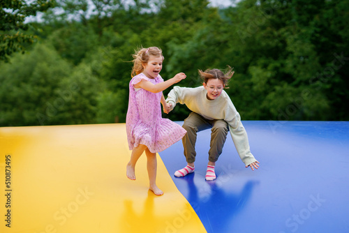 Little preschool girl and school sister jumping on trampoline. Happy funny children, siblings in love having fun with outdoor activity in summer. Trampolin in ukrainian flagg colors