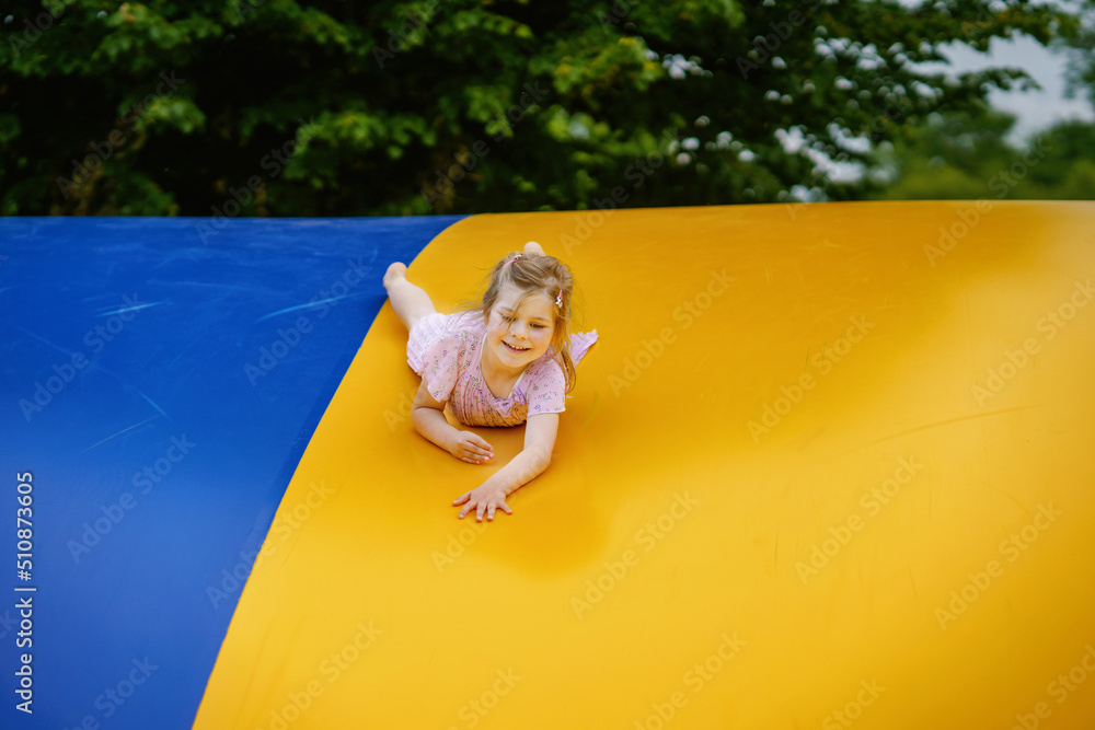 Little preschool girl jumping on trampoline. Happy funny toddler child having fun with outdoor activity in summer. Sports and exercises for children. Trampolin in ukrainian flagg colors