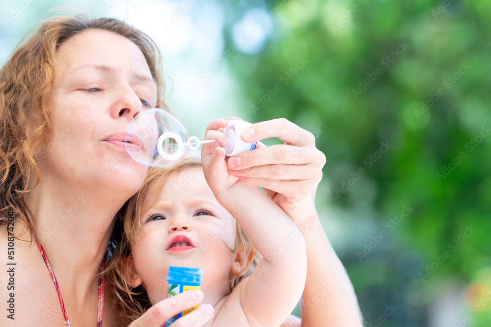 Little girl plays with soap bubbles. Mom and daughter by the pool. Fun summer day with family. Happy child blowing bubbles Little girl plays with soap bubbles. Mom and daughter by the pool. Fun summer day with family. Happy child blowing bubbles