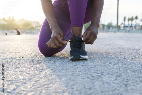 Crop black woman tying shoelaces on sneakers in street photo