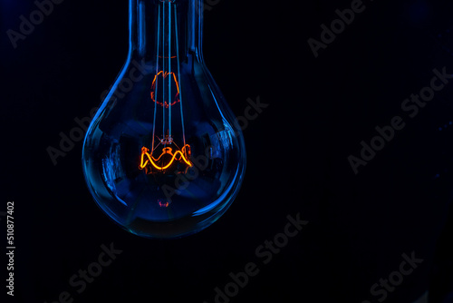 Glowing lamp, tungsten light bulb lit on black background,  close up shot, on wood table,  idea concept,  natural wax candle, Burning candle near a switched off light bulb in complete darkness.