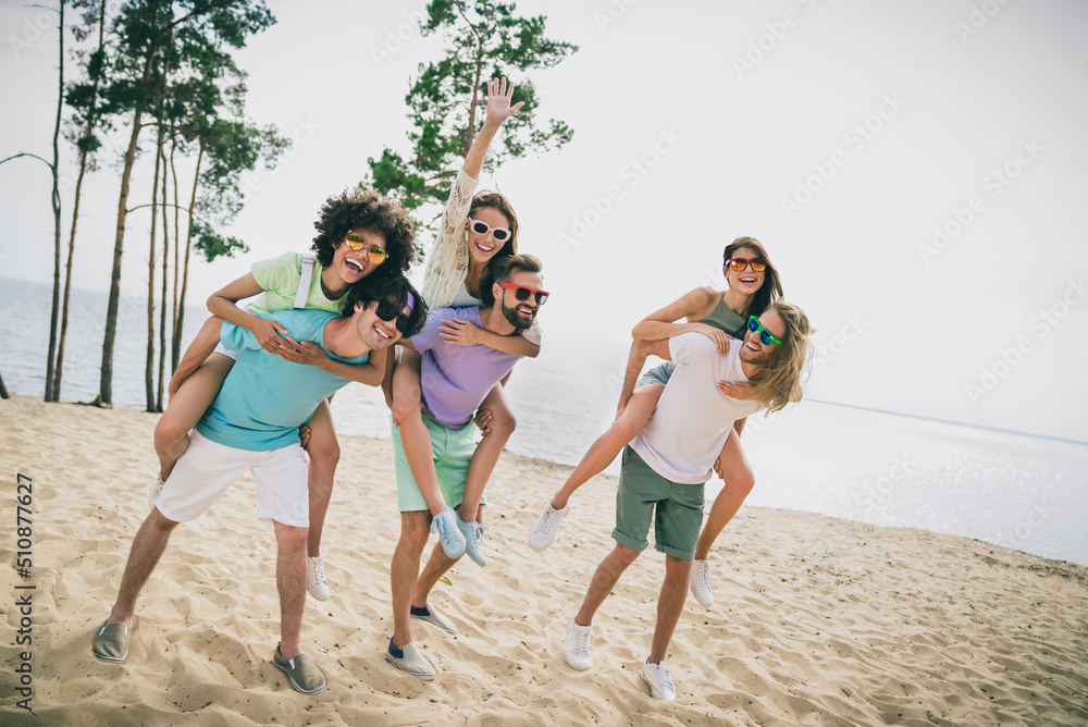 Full body portrait of excited positive friends have fun hanging out piggyback ride sand beach outdoors Full body portrait of excited positive friends have fun hanging out piggyback ride sand beach outdoors