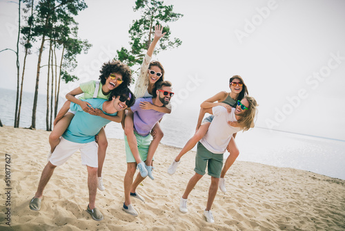 Full body portrait of excited positive friends have fun hanging out piggyback ride sand beach outdoors