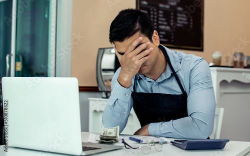 Business restaurant or cafe owner or entrepreneur getting stress, put hands on head with sad and suffer from bad economics and lost profit while sitting in front of laptop, calculating less income.