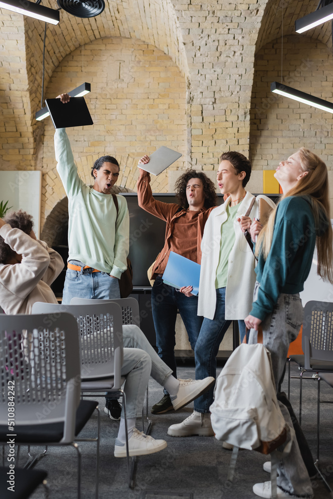 excited multiethnic students with closed eyes showing win gesture in auditorium. excited multiethnic students with closed eyes showing win gesture in auditorium.