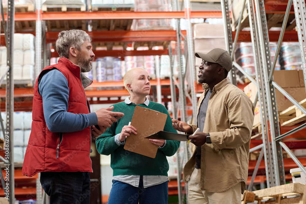 African young worker discussing cargo delay with his colleagues during their teamwork in warehouse