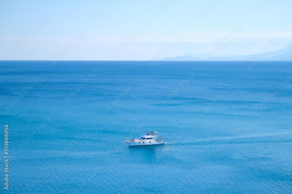 White yacht floats on blue water in the sea against the backdrop of mountains on a sunny day