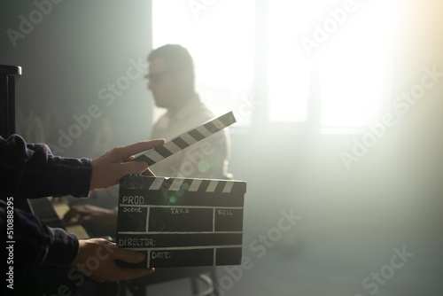 Clapperboard or clipboard in hands. Guy is directing and filming retro cinema or vintage movie. Composer man play on the old piano. photo