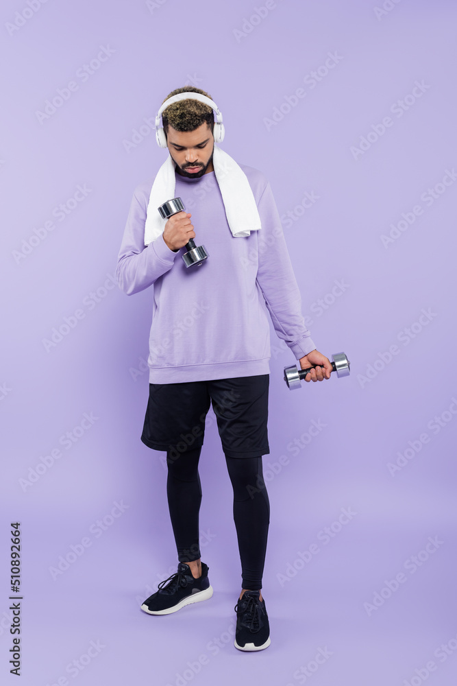 full length of bearded african american man in headphones exercising with dumbbells on purple. full length of bearded african american man in headphones exercising with dumbbells on purple.