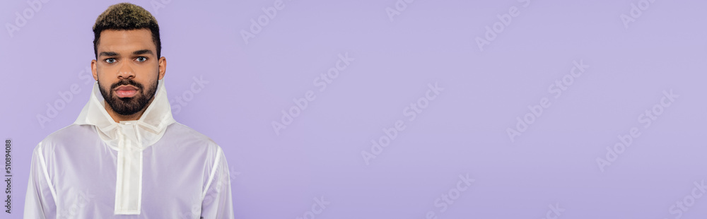 Fototapeta premium young african american man in trendy sportswear looking at camera isolated on purple, banner.