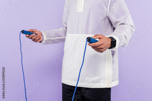 cropped view of african american man in trendy sportswear holding skipping rope isolated on purple.