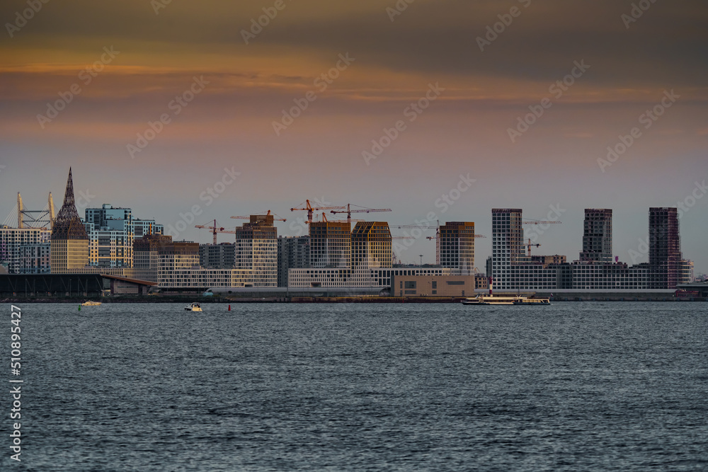 The residential complex under construction on the embankment of the Neva River on Vasilievsky island in sunset, bulk island, construction cranes