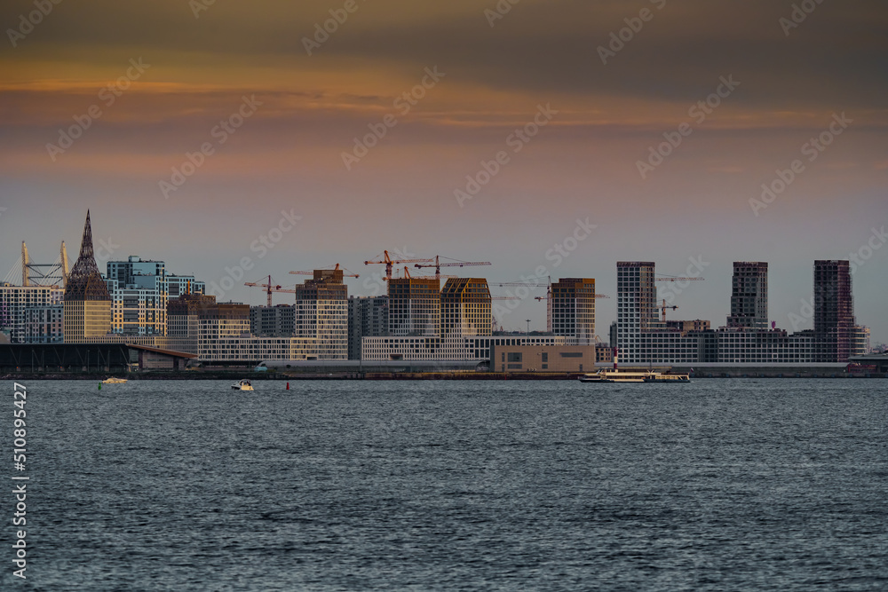 Fototapeta premium The residential complex under construction on the embankment of the Neva River on Vasilievsky island in sunset, bulk island, construction cranes