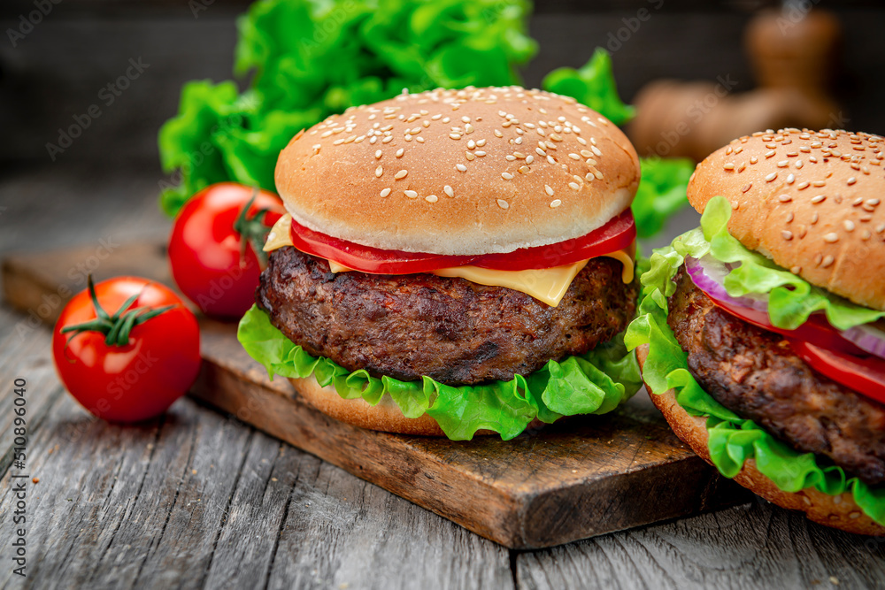 Two delicious homemade burgers of beef on an old wooden table. Fat unhealthy food close-up. Two delicious homemade burgers of beef on an old wooden table. Fat unhealthy food close-up.
