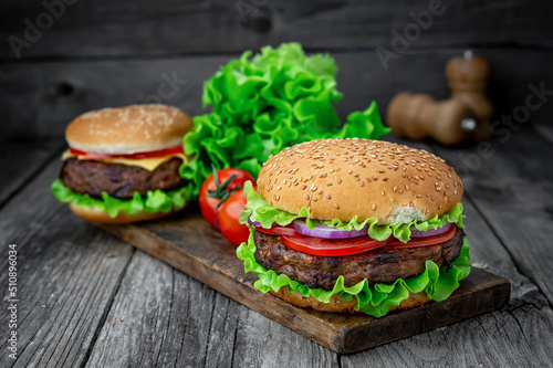 Two delicious homemade burgers of beef on an old wooden table. Fat unhealthy food close-up.