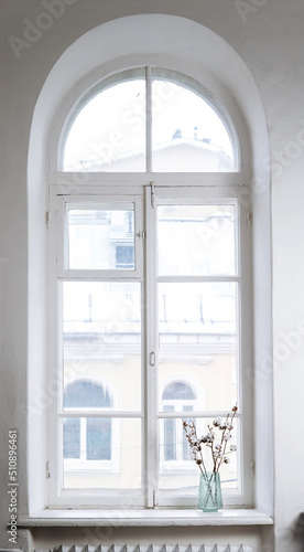 White fluffy cotton swabs in full bloom. Several branches of cotton are in a vase on the windowsill. Large old window.