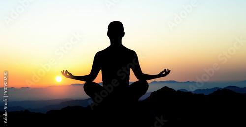 Silhouette of man in yoga lotus pose on top of mountain. Meditation and astrology. Esoterica and psychology. Landscape in sunrise. Elements of this image furnished by NASA