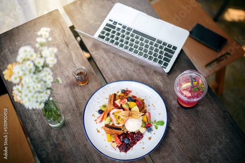 top view of laptop and smartphone  with French toast topping mixed fruit , ice cream , italian soda on wooden table in modern bright kitchen interior
