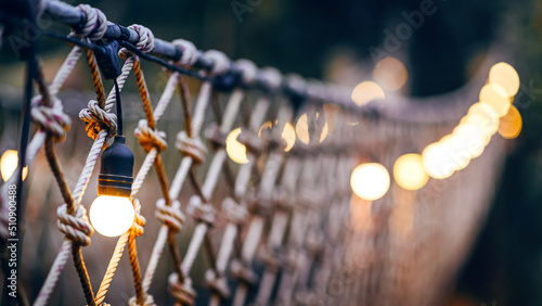 Fotografiet rope bridge decorated with warming bulb light at twilight evening