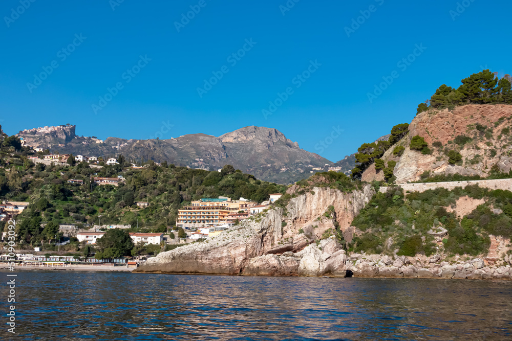 Touristic boat tour with panoramic view from open sea on the Mediterranean coastline near Isola Bella in Taormina, Sicily, Italy, Europe, EU. Calm water surface at Ionian Mediterranean sea