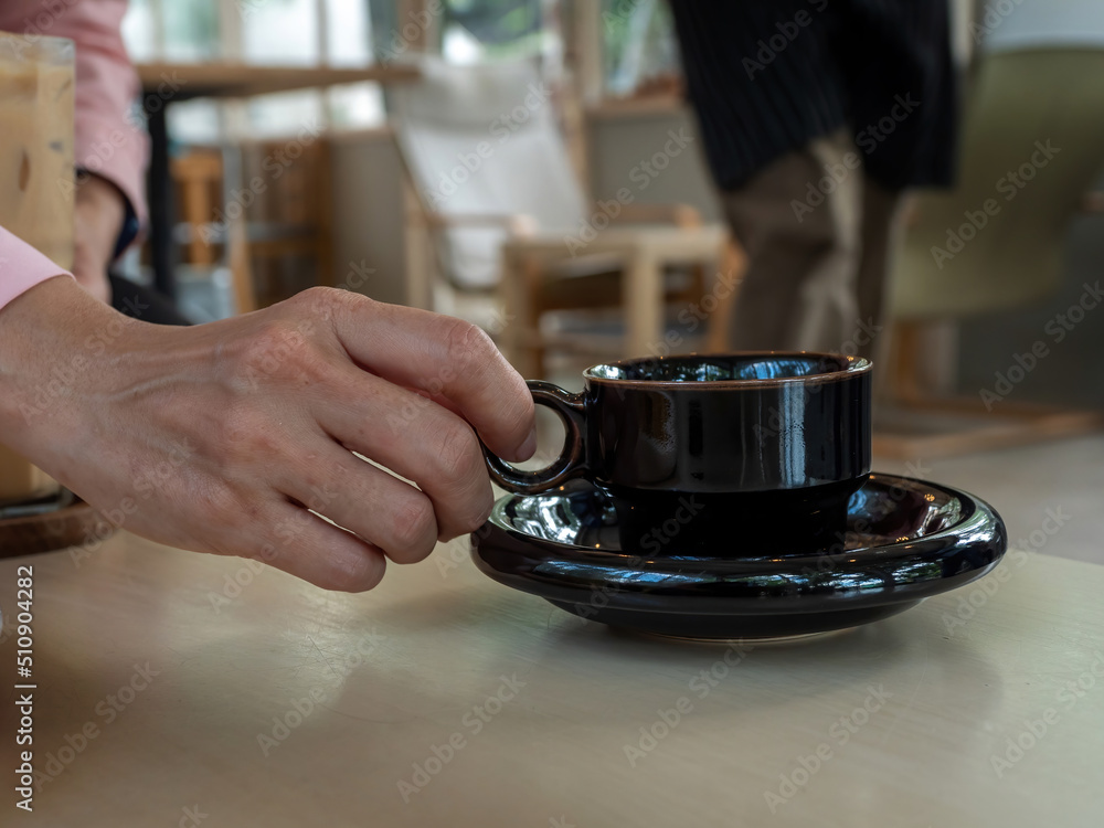 Close up female hand holding black color coffee cup in the coffee shop. Close up female hand holding black color coffee cup in the coffee shop.