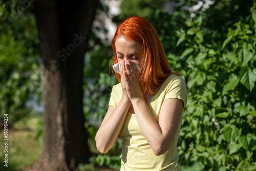 Young redhair woman sneezing in park. Pollen Allergy symptoms