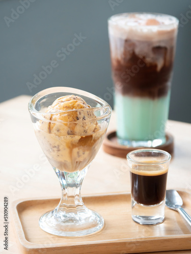 Close up , Affogato, Italian coffee-based dessert in small wooden tray. It has a scoop of chocolate chip ice cream with shot of hot espresso. Blurry background of a glass of chocolate mint.
