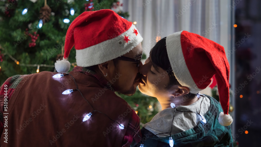 Happy gay couple kissing, sharing a romantic moment together on Christmas Eve. Asian LGBTQ lovers celebrating special day together.