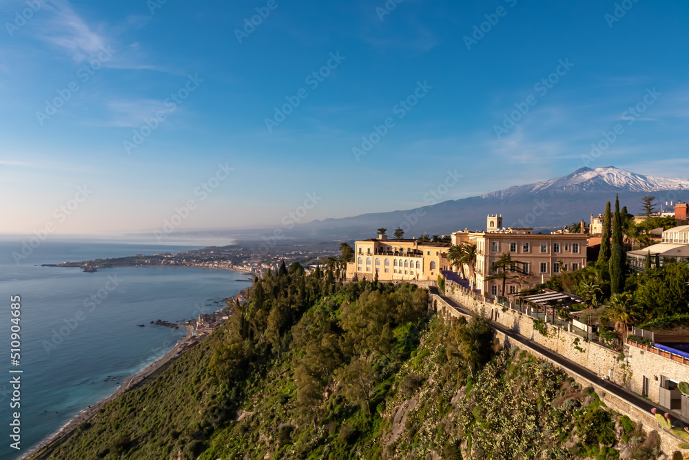 Luxury San Domenico Palace Hotel with panoramic view on snow capped Mount Etna volcano seen from public garden Villa Comunale in Taormina, Sicily, Italy, Europe, EU. Coastline Ionian Mediterranean sea