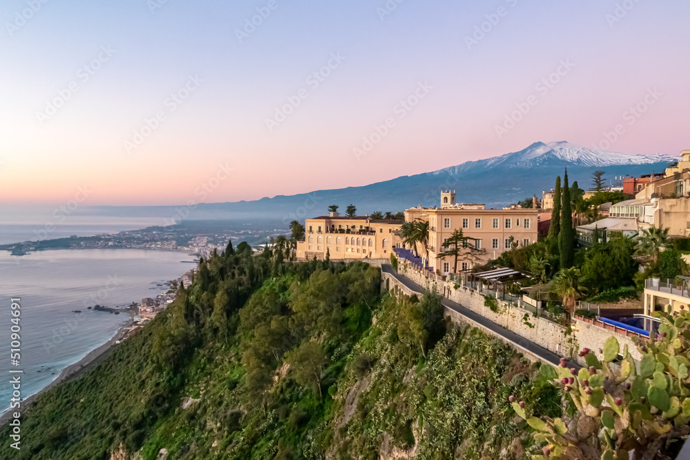 Luxury San Domenico Palace Hotel with panoramic view on snow capped Mount Etna volcano seen from public garden Villa Comunale in Taormina, Sicily, Italy, Europe, EU. Coastline Ionian Mediterranean sea