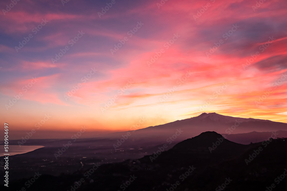 Panoramic view on silhouette of hills during twilight. Watching beautiful sunset behind volcano Mount Etna near Castelmola, Taormina, Sicily, Italy, Europe, EU. Clouds with vibrant red orange colors