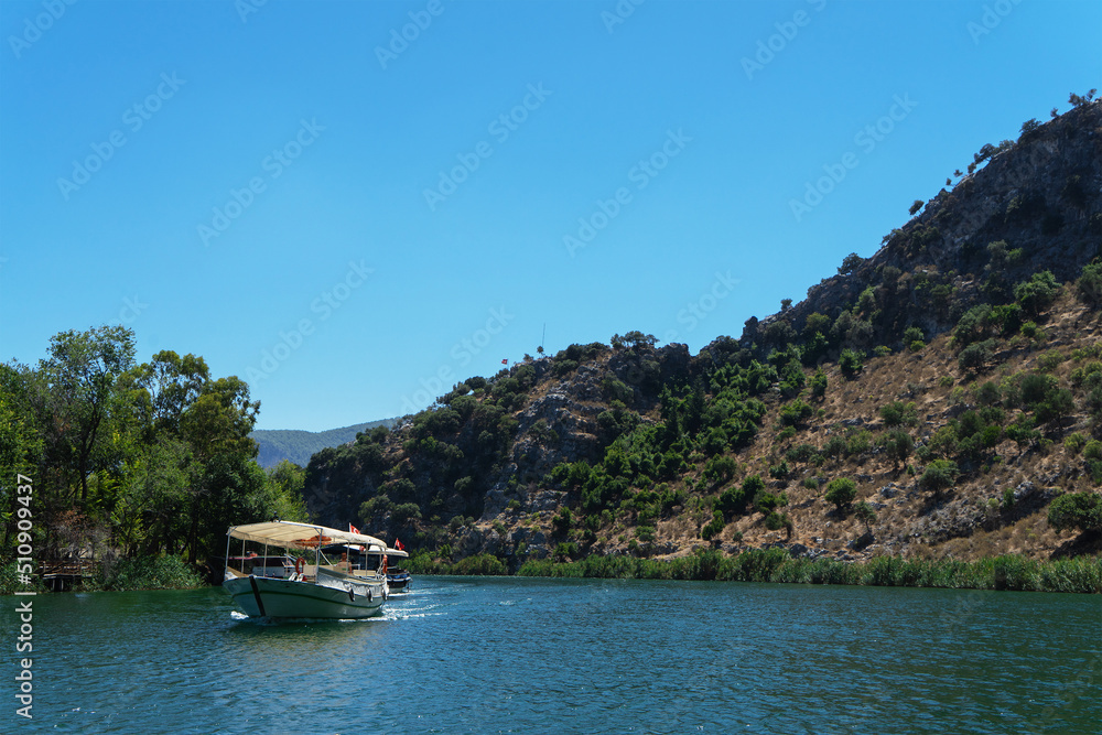 Pleasure ships under Turkish flags on the Dalyan River, Turkey against the background of rocks and trees on a sunny summer day