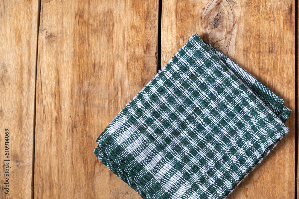A green checkered cloth lies against a wooden background. A towel or kitchen napkin on the rough boards or kitchen table. A green checkered cloth lies against a wooden background. A towel or kitchen napkin on the rough boards or kitchen table.