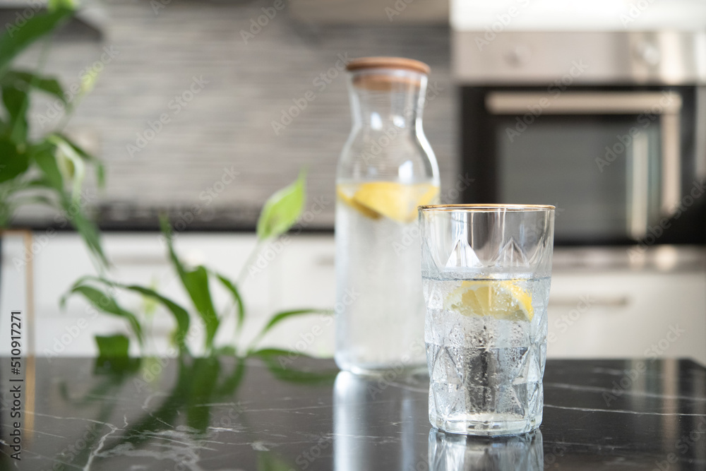 Glass with homemade lemonade in the kitchen. Summer refreshing lemonade drink. Water with lemon. Glass with homemade lemonade in the kitchen. Summer refreshing lemonade drink. Water with lemon.