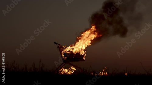 A man puts out a burning supermarket cart with a fire extinguisher in an empty field, against the background of a golden sunset closer to the dark night, slow motion