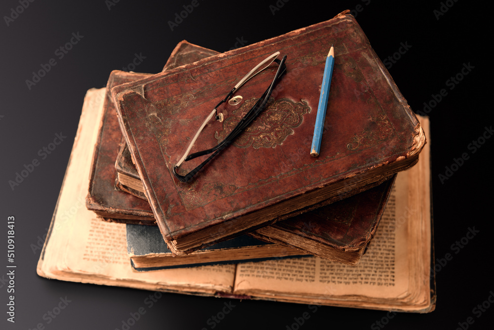 Stack of old worn jewish books in leather binding on open Torah pages on dark background. Closeup. Selective focus.