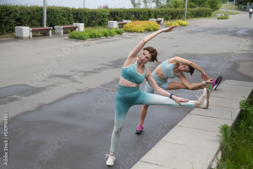 Sporty two woman in sports outfit doing morning workout and stretching on street sports ground. Fitness workout on the sports ground. training with an insructor in nature  photo