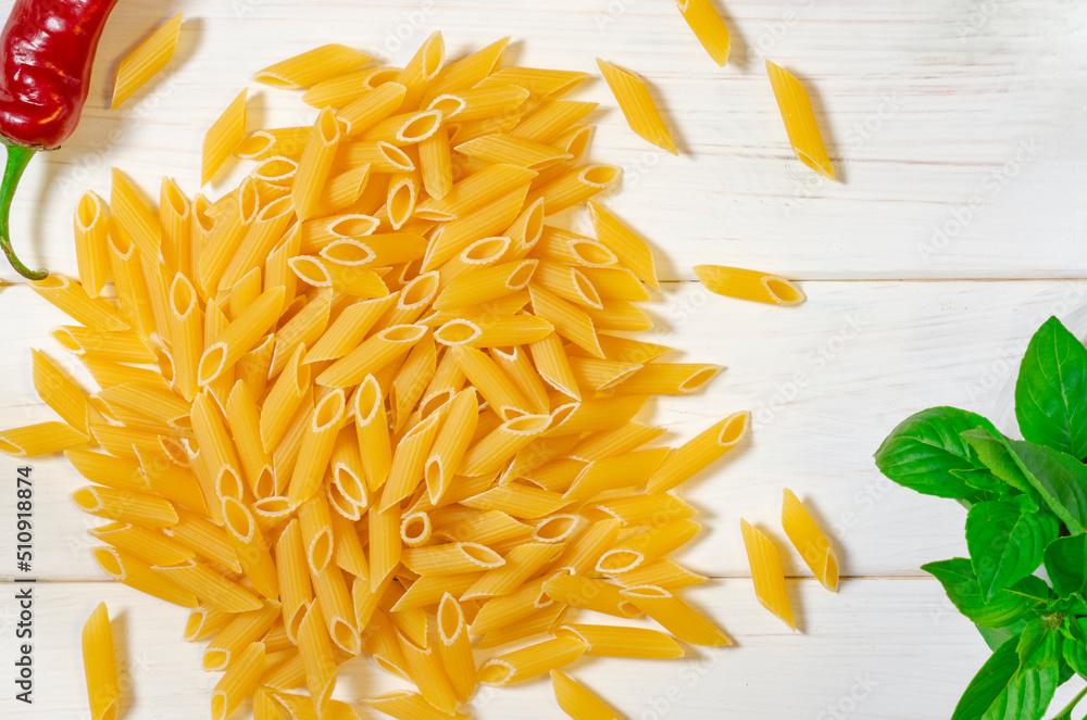 Fototapeta premium Penne Pasta, green basil, parmesan, sesame, garlic, chilli, eggs lie on a white tree table